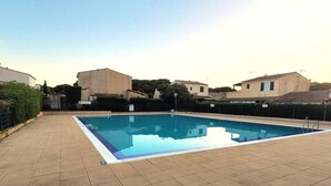 A swimming pool with a tiled deck, surrounded by buildings and greenery. - Air-conditioned T3 Villa for 6 with pool and parking in Cap d'Agde (Cap d'Agde)