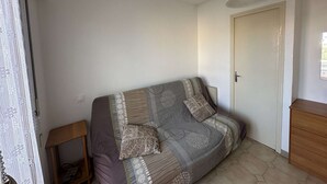 A small, neatly arranged room with a single sofa, a wooden side table, and a door. - Studio near beach with terrace in L'Ile-Rousse (L'Île-Rousse)