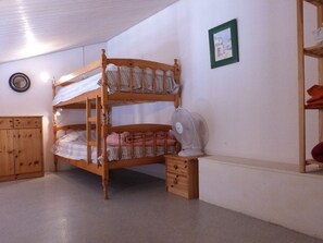Ein Schlafraum mit Etagenbetten, einem Holzkopfteil, einem Nachttisch mit Ventilator und einem Holzschrank.