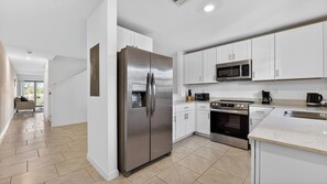 A modern kitchen with white cabinets, stainless steel appliances, and a herringbone floor pattern. - Sunny Escape | Fresh, Modern Townhome Near Beaches (Port Charlotte)