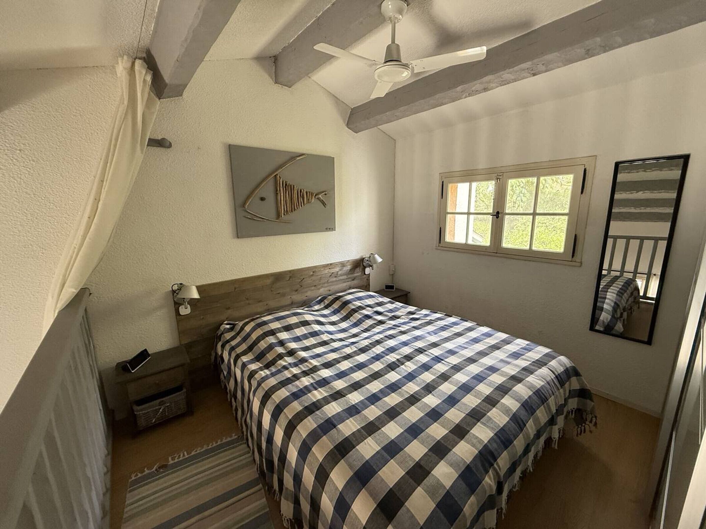 A bedroom with a bed, a ceiling fan, a window, a wall-mounted fish artwork, and a mirror.