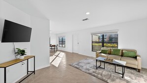 A spacious living room with a flat-screen TV, a sofa with green cushions, and a dining area in the background. - Sunny Escape | Fresh, Modern Townhome Near Beaches (Port Charlotte)