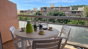 Een balkon met een ronde tafel gedekt voor twee personen, met een groene waterkoker, twee kopjes en een kleine plant.