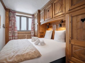 A room with a bed, wooden paneling, a window with curtains, and a wall-mounted lamp. - Renovated ski-in ski-out apartment for 7 people (Courchevel 1850)