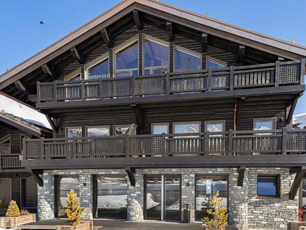 A two-story log cabin with a balcony, stone foundation, and large windows. - Renovated ski-in ski-out apartment for 7 people (Courchevel 1850)