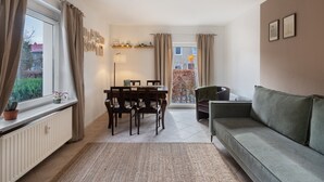 A living room with a sofa, a dining table with chairs, a radiator, and a window with curtains. - Apartment 'Yvette's 2' with Shared Garden and Wi-Fi (Lugau/Erzgeb.)