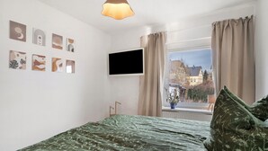 A bedroom with a bed, a TV mounted on the wall, and a window with curtains. - Apartment 'Yvette's 2' with Shared Garden and Wi-Fi (Lugau/Erzgeb.)