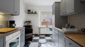 A kitchen with grey cabinets, a wooden countertop, a built-in oven, a coffee maker, and a window with a view of a brick building. - Apartment 'Yvette's 2' with Shared Garden and Wi-Fi (Lugau/Erzgeb.)