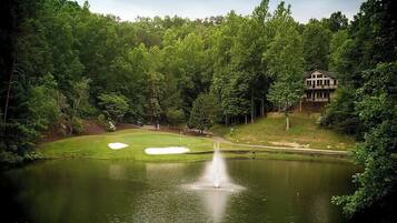 A golf course with a pond, a fountain, and a building in the background.