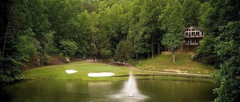 A golf course with a pond, a fountain, and a building in the background.