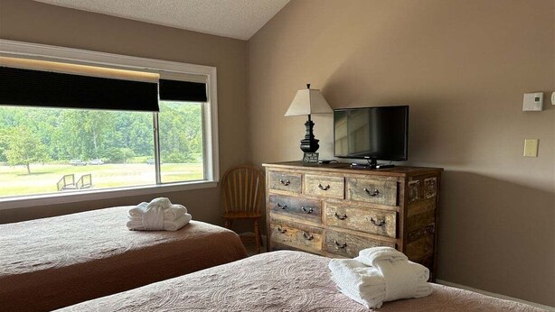 Ein Hotelzimmer mit zwei Betten, einem Holzschrank, einem Fernseher und einem Fenster mit Jalousien.
