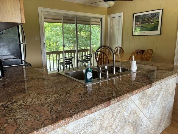 A kitchen with granite countertops, a stainless steel sink, and a dining area with chairs.