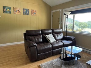 A brown leather sofa with a pillow, a small round table, and three bird paintings on the wall.