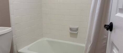 Une salle de bain avec des toilettes blanches, une baignoire et un rideau de douche.