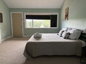 A bedroom with a bed, a window, a door, and a wall-mounted picture.