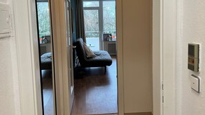 Ein schmaler Flur führt zu einem Schlafzimmer mit einem Bett, einem Fenster und einem Spiegel.