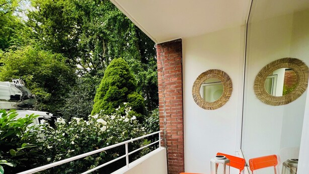 Ein Balkon mit Tisch und Stühlen, einer Laterne und Blick auf Grünflächen sowie ein Fahrzeug.