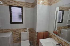 Een badkamer met witte tegels, een toilet, een wastafel en een spiegel.