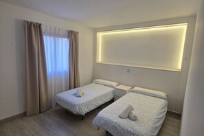 Een hotelkamer met twee enkele bedden, een groot raam met gordijnen en een wandlamp.