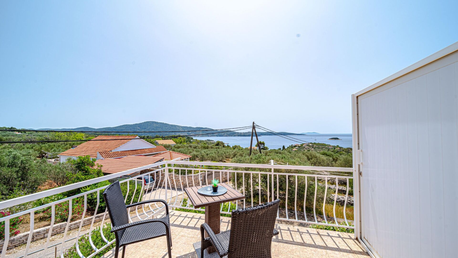 Un balcón con una mesa y dos sillas, con vistas a un paisaje costero con casas y un puente.