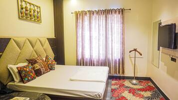 A hotel room with a bed, a TV mounted on the wall, a window with curtains, and a decorative wall piece.