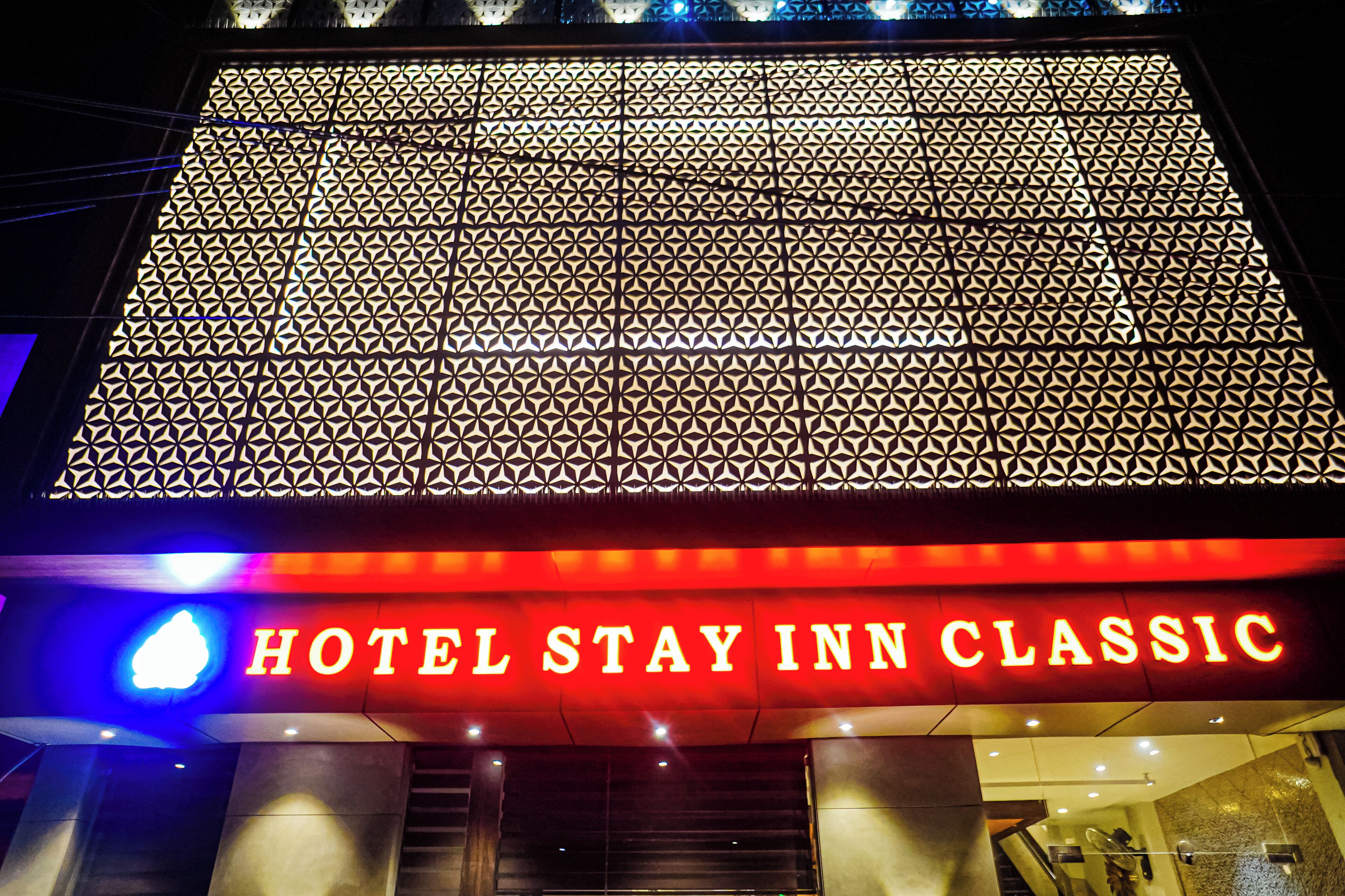 A hotel entrance with a geometric patterned facade and a prominent illuminated sign reading "HOTEL STAY INN CLASSIC".