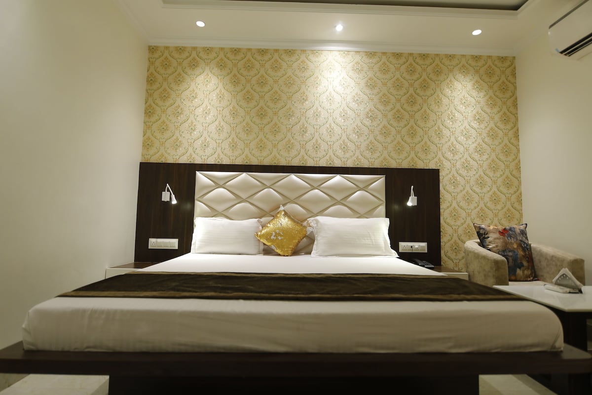 A hotel room with a large bed, a headboard with a diamond pattern, two bedside tables with lamps, and a patterned wallpaper on the wall.