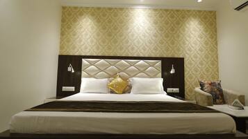 Quarto de hotel com uma cama grande, cabeceira com padrão de losangos, duas mesas de cabeceira com luminárias e papel de parede estampado na parede.