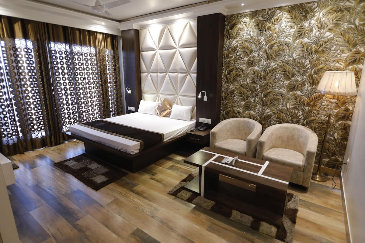 A modern bedroom with a large bed, two armchairs, a nightstand, and a decorative wall.