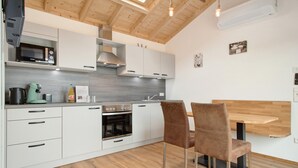 Una cocina moderna con armarios blancos, horno integrado, microondas y un comedor con dos sillas.
