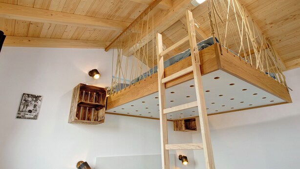 Una habitación estilo loft con techo de madera, una cama en un entrepiso, una escalera y un pequeño estante de madera.