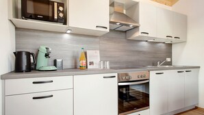 Una cocina moderna con armarios blancos, horno integrado, microondas y cafetera.