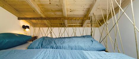Een kamer met een houten plafond, een bed met blauw beddengoed en een wandlamp.
