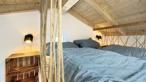 Une chambre avec un plafond en bois, un lit avec une literie grise et un luminaire suspendu.