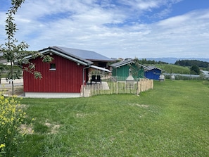 Une grange rouge avec un porche abrité, un bâtiment vert doté d’une cheminée et un bâtiment bleu situé dans un champ verdoyant.