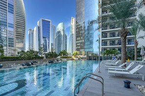 Una piscina con sillones de descanso y palmeras, rodeada de edificios altos.
