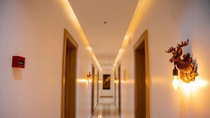 A hotel hallway with a wooden floor, wall-mounted light fixtures, and a red emergency exit sign. - De-Oma Villa Hotel And Apartment (Benin City)