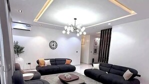 A modern living room with a sectional sofa, a coffee table, and a chandelier. - De-Oma Villa Hotel And Apartment (Benin City)