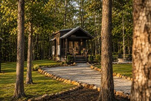 A cabin with a porch, surrounded by trees and a gravel path. - Hickory Hideaway at The Retreat at Deer Lick Falls (Monteagle)