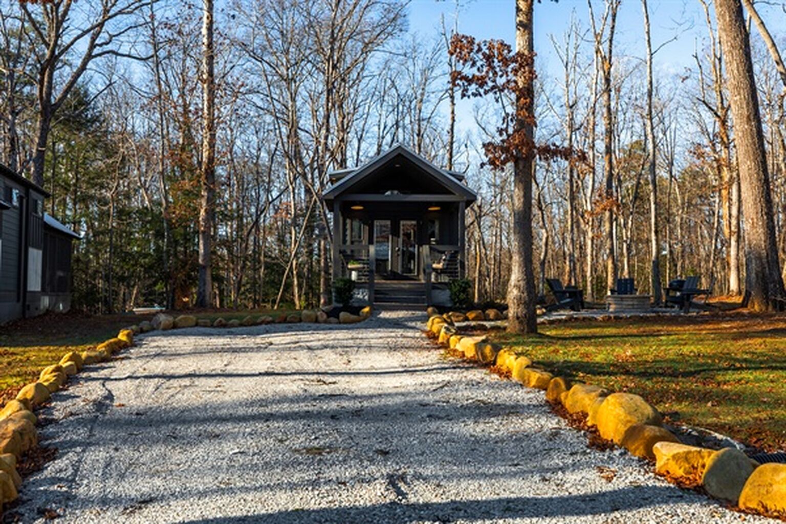 A lodge with a gravel driveway leading to a covered entrance, surrounded by trees and a park area.