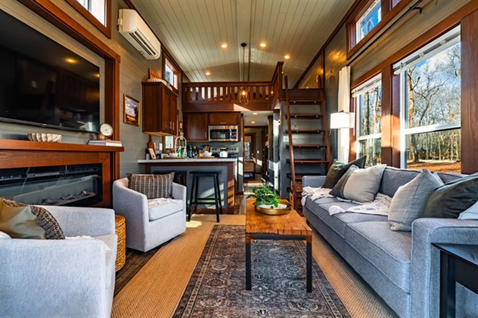 A spacious living area with a fireplace, a sofa, a coffee table, and a kitchen in the background.