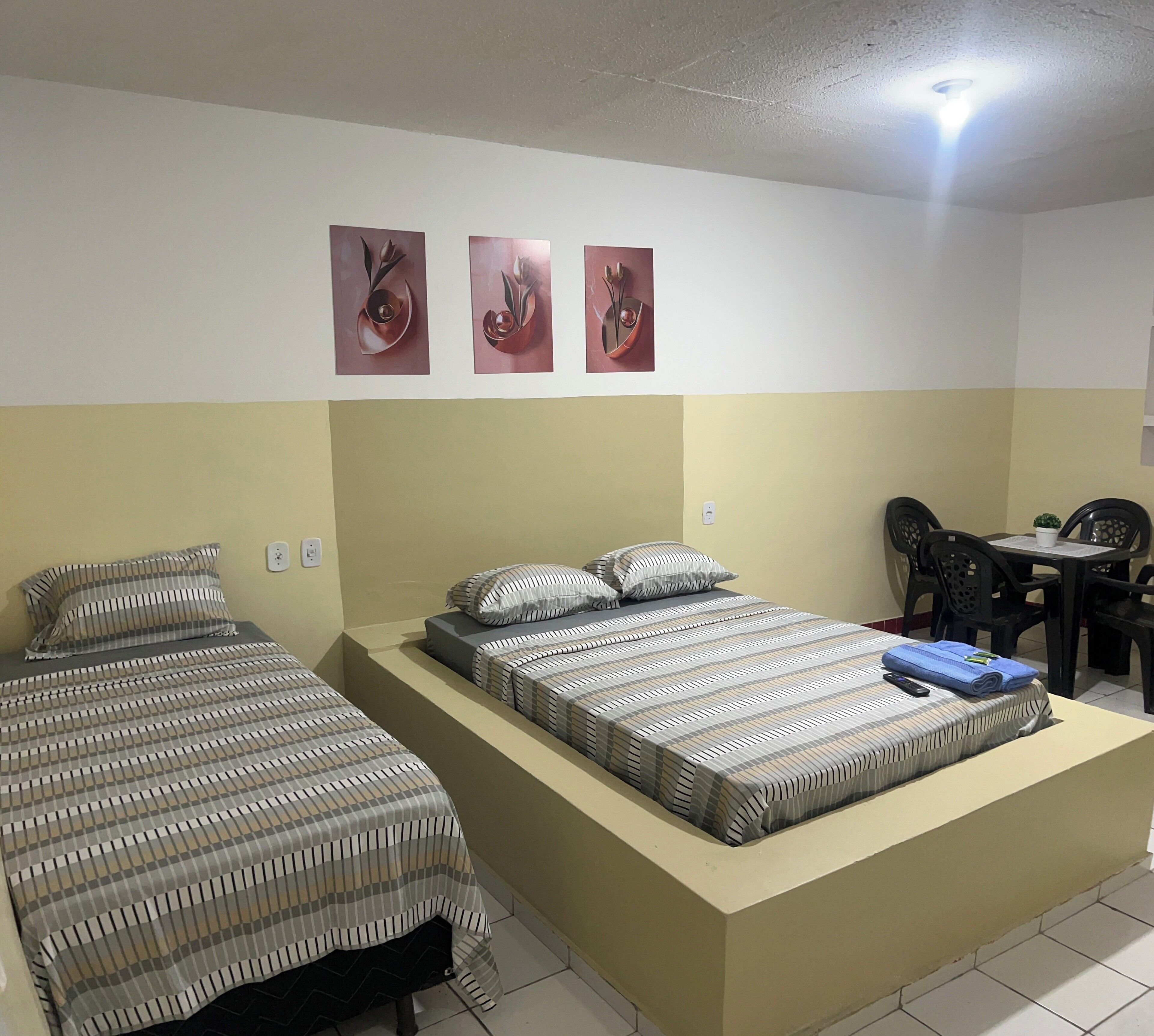 A room with two beds, a small table, and chairs. There are three wall-mounted pictures.