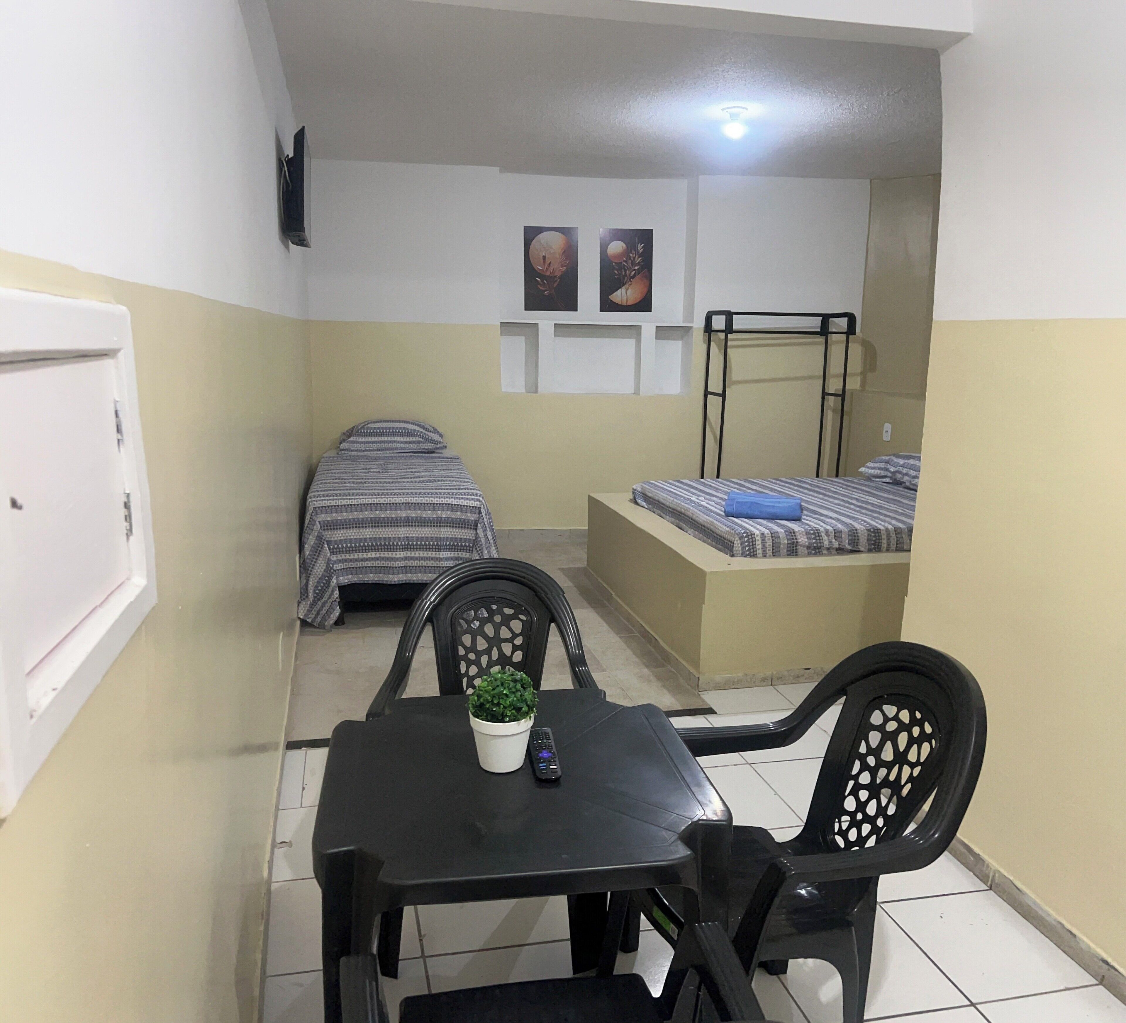 A compact room with a bed, a small table with a plant, and a chair.