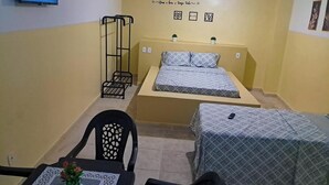 A small, compact room with two beds, a TV, a chair, and a table with a vase. - POUSADA SOLAR DOS LUSITANOS (São Luís)