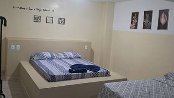 Un dormitorio con una cama, una mesita de noche, un estante en la pared y otra mesita más pequeña.