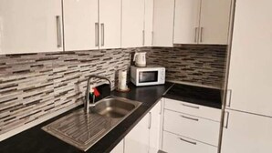 Una cocina moderna con armarios blancos, una encimera negra, un fregadero de acero inoxidable y un microondas.
