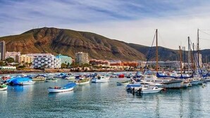 Una marina con barcos amarrados, montañas al fondo y edificios en primer plano.