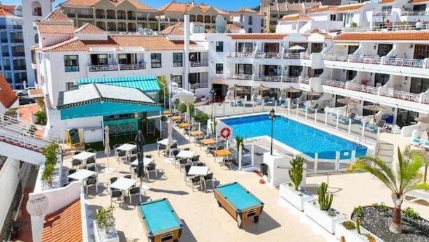 Un resort con piscina, mobiliario exterior y varios balcones.