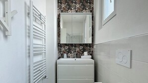 A modern bathroom with a white vanity, a toilet, and a radiator.