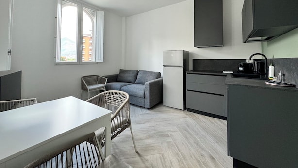 A modern kitchen with a built-in stove, a dining area with a table and chairs, and a grey sofa.